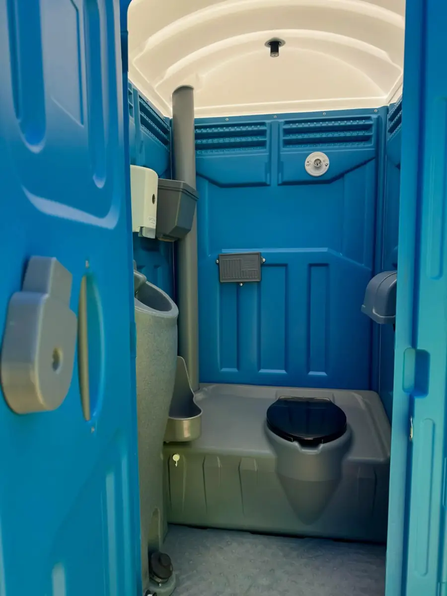 Inside a deluxe porta potty with a corner sink, mirror and toilet